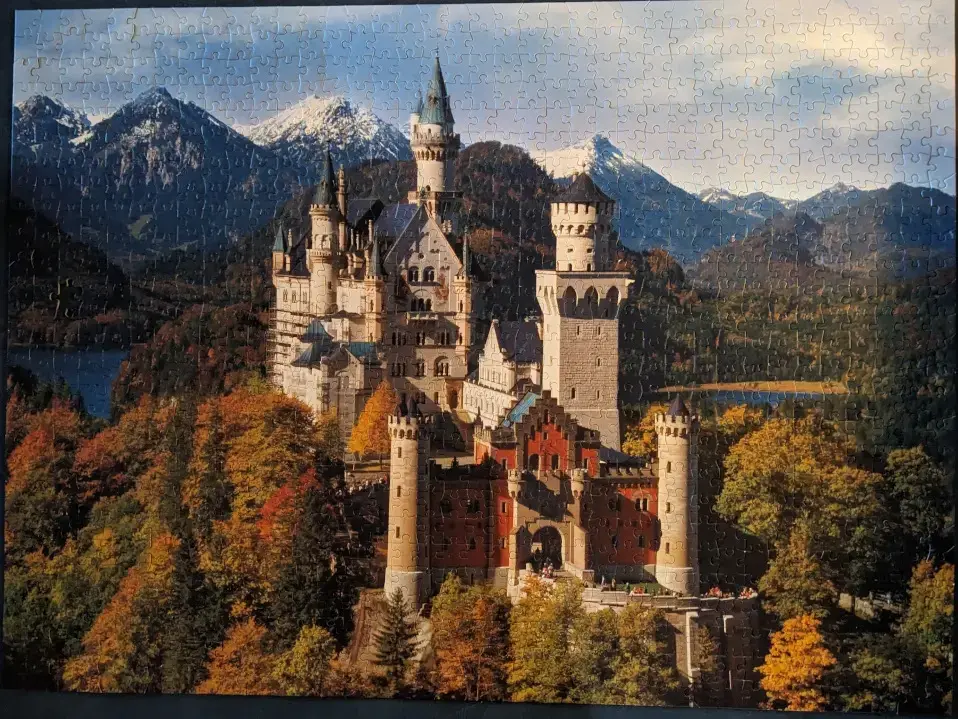 A slightly skewed photograph of an assembled jigsaw puzzle showing the Neuschwanstein castle during the fall with vibrant changing leaf colors