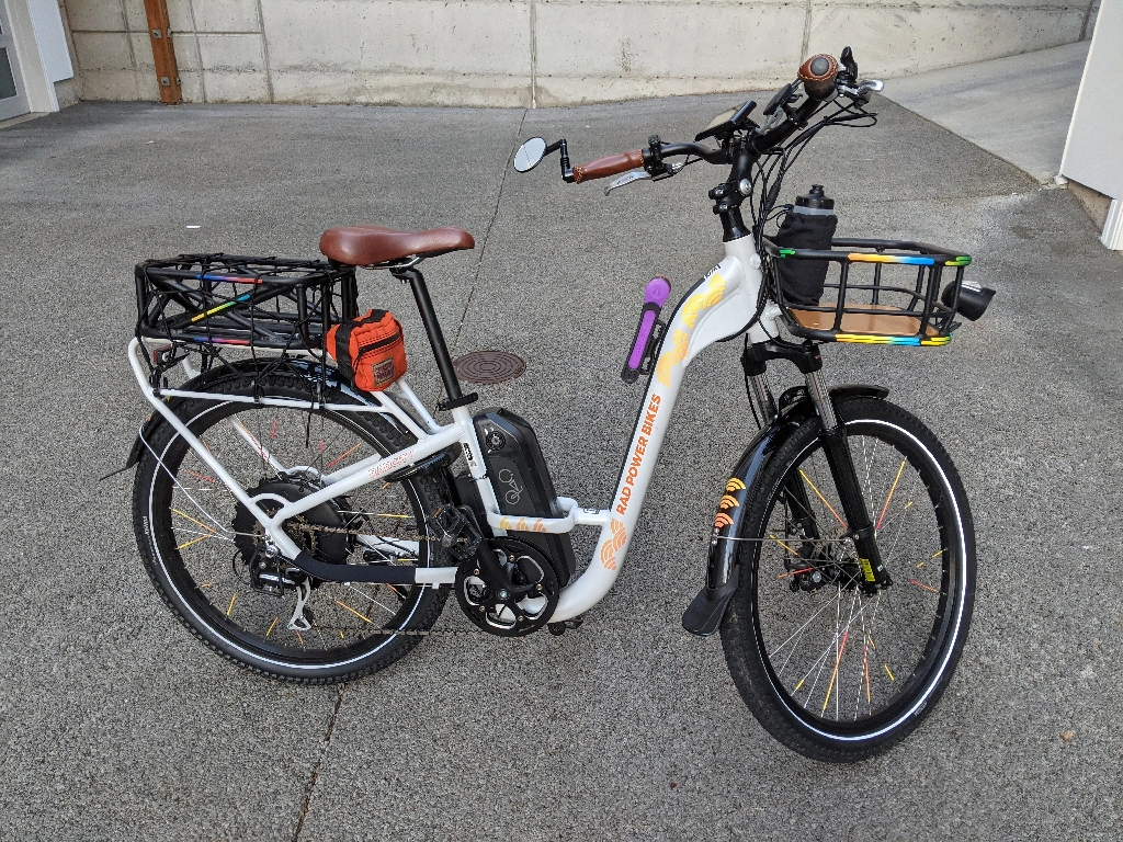 A white step-thru Ebike with front and rear baskets and lots f reflective stickers. 
