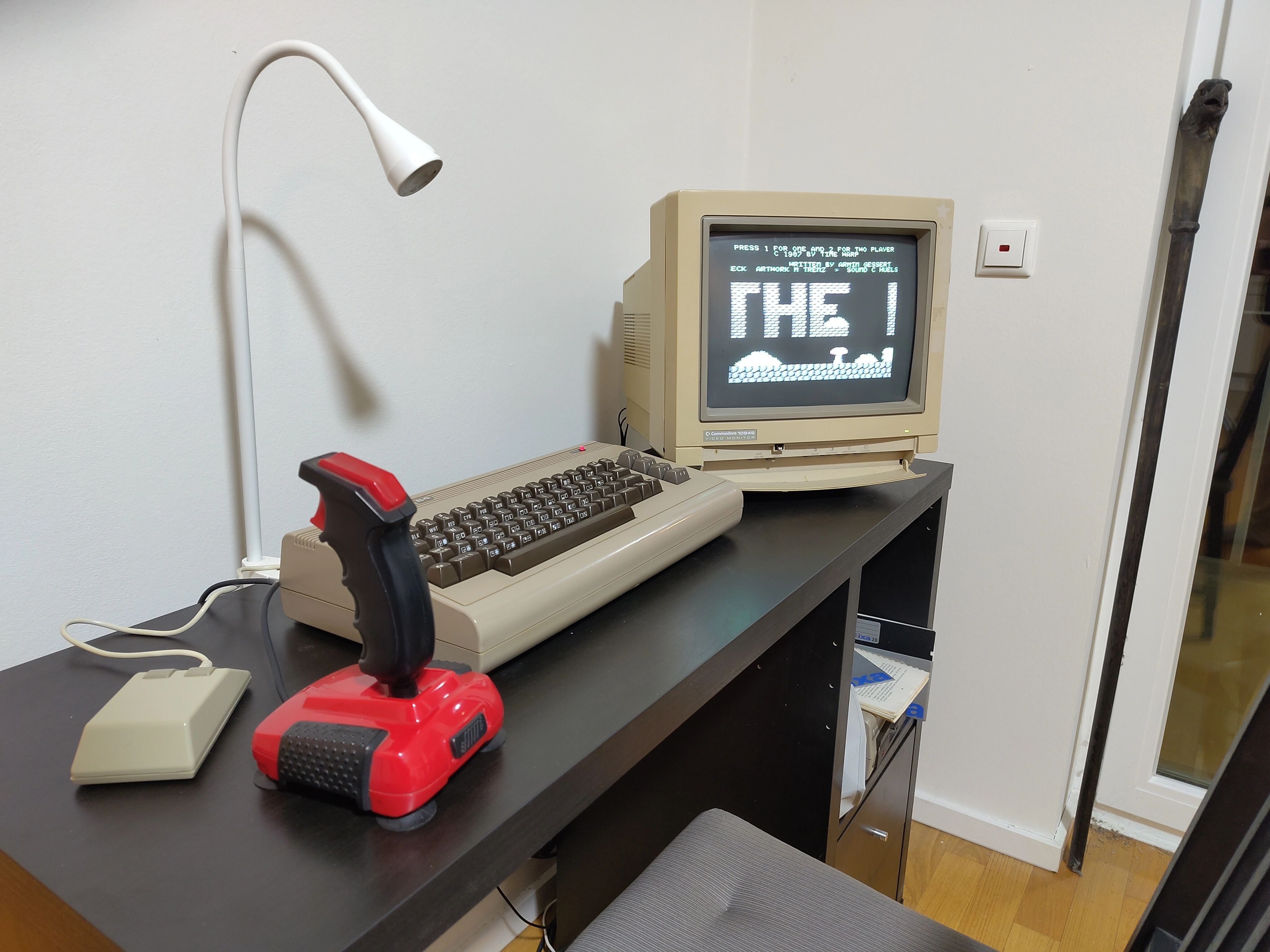 a clean desk with several C64 peripherals e.g. a mouse, quickshot 2, the commodore 64 itself and a commodore 1084S colour monitor.