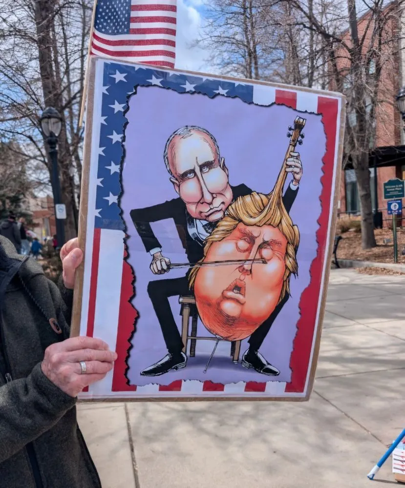 A protest sign showing Putin playing a Cello in the form of Trump's face