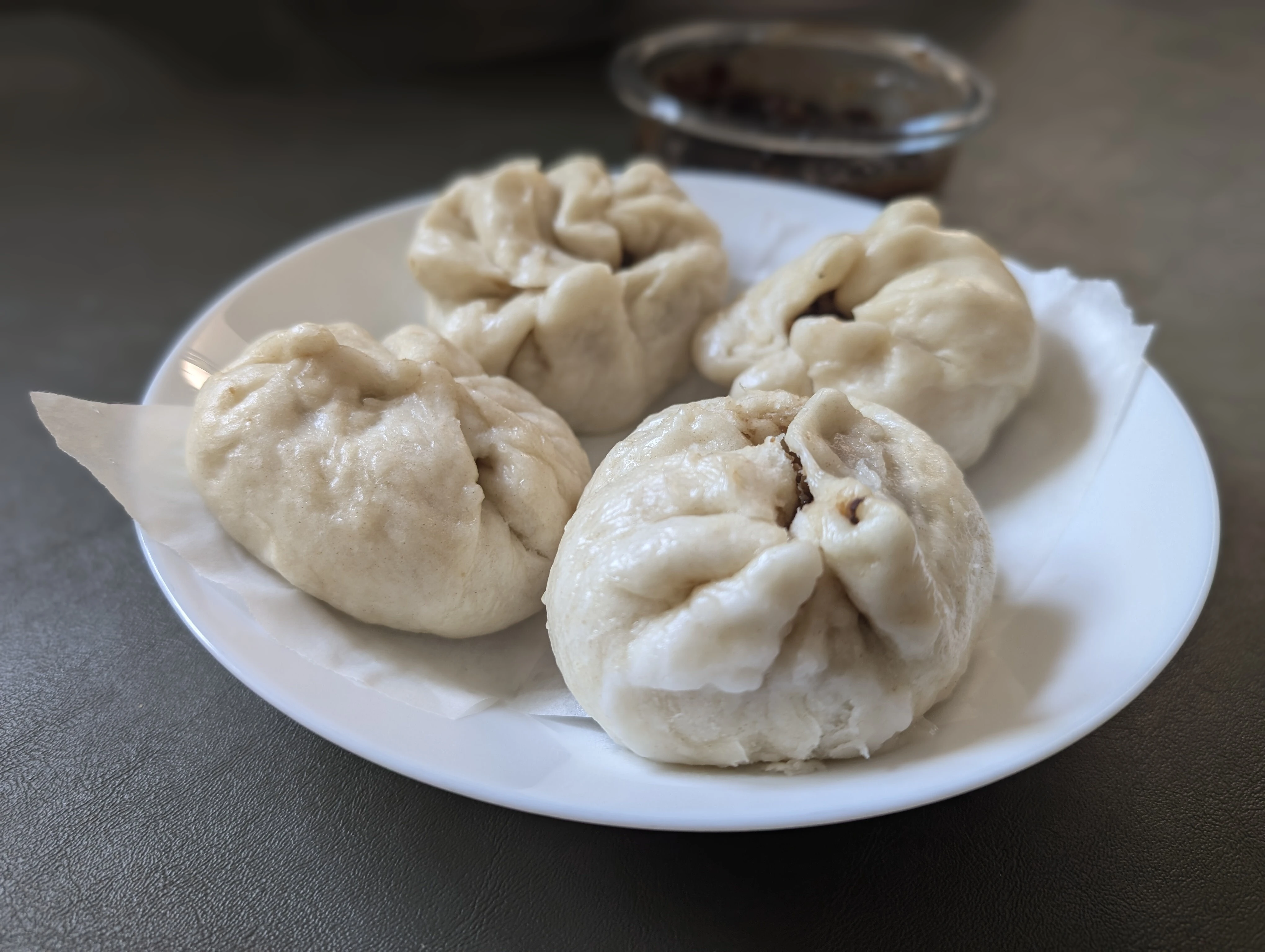 four siopao (steamed buns) arranged on a white plate.