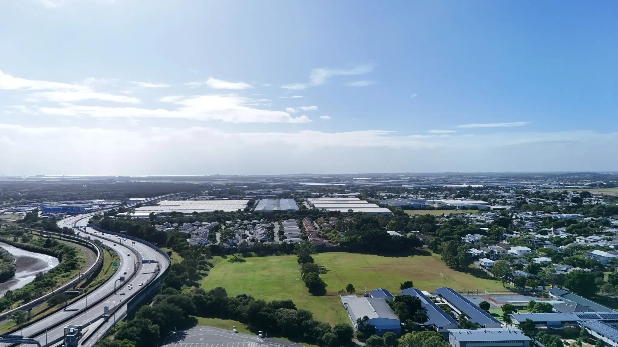 An ariel photograph looking out over Hendra, towards Pinkenba and the ocean. The sky is blue, with some fluffy white clouds, and a bright sun
