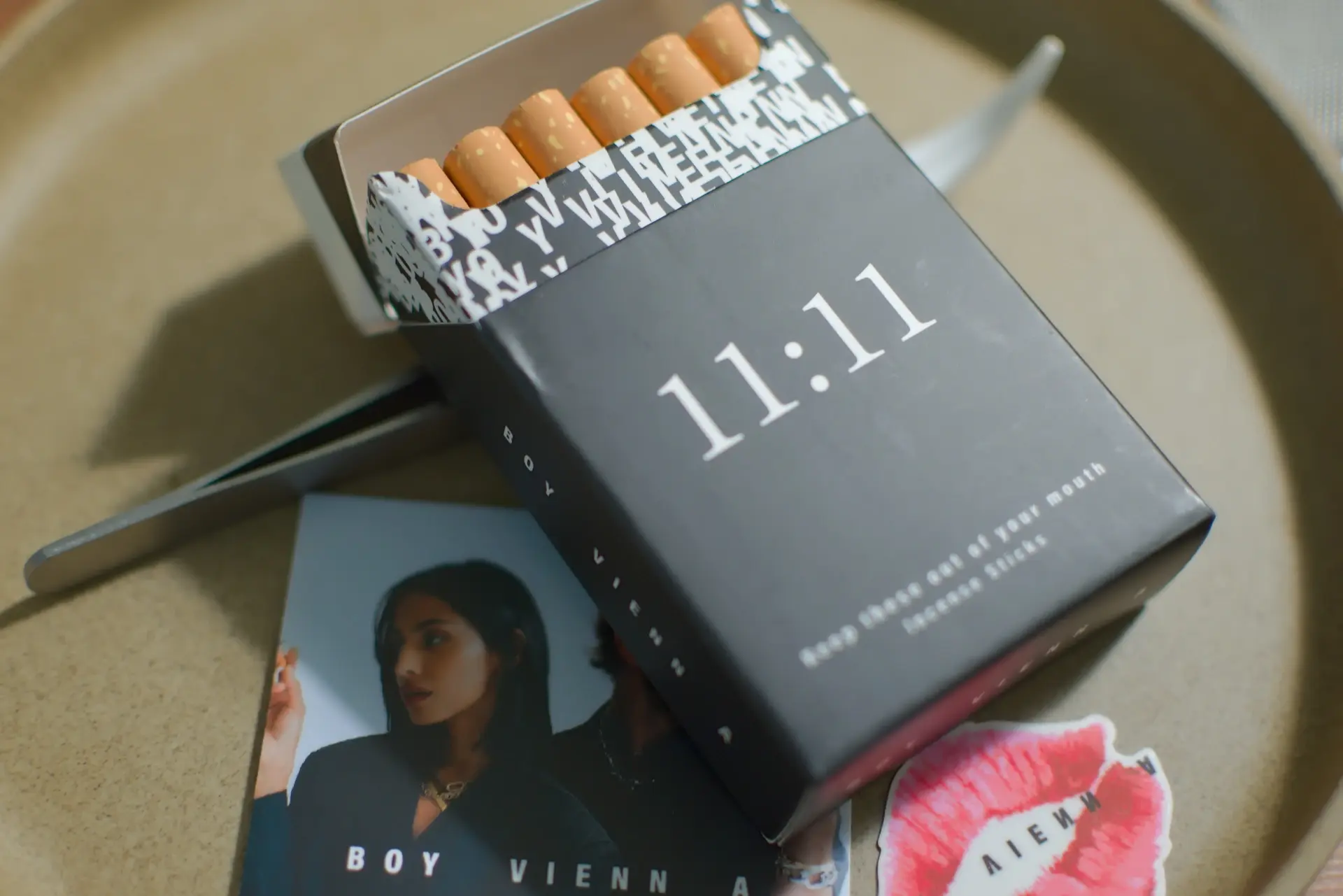 What appears to be a pack of cigarettes labeled 11:11. There is also a card featuring the brand name Boy Vienna and a temporary tattoo featuring an image of a lipstick-print and the brand name.