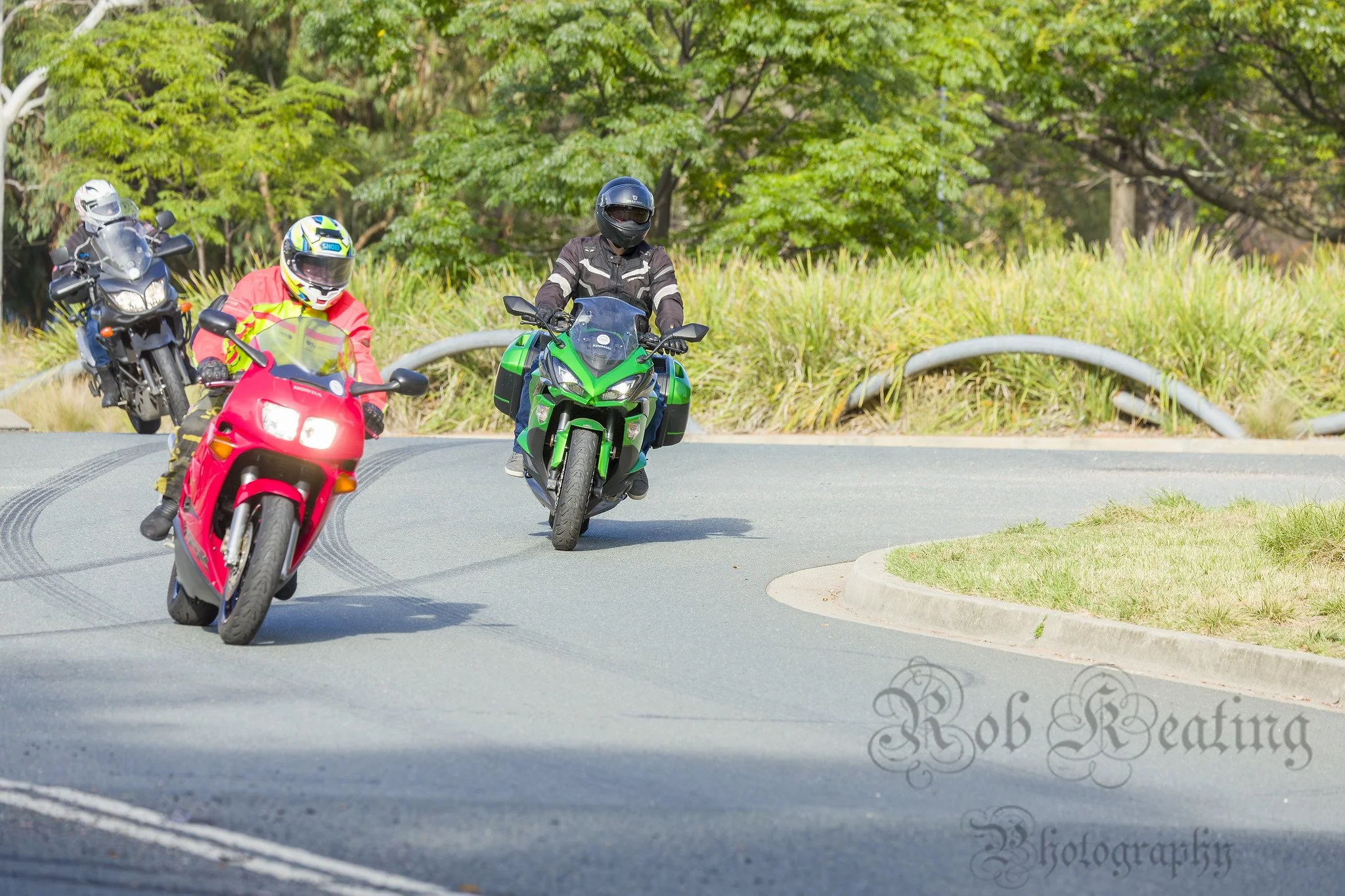 Three motorcycles taking a corner at low speed, a red Honda with a rider in high-vis gear, a lime green Kawasaki Ninja 100 with the rider in black gear and a blue Yamaha XT1200 with a rider in a black jacket and white helmet.