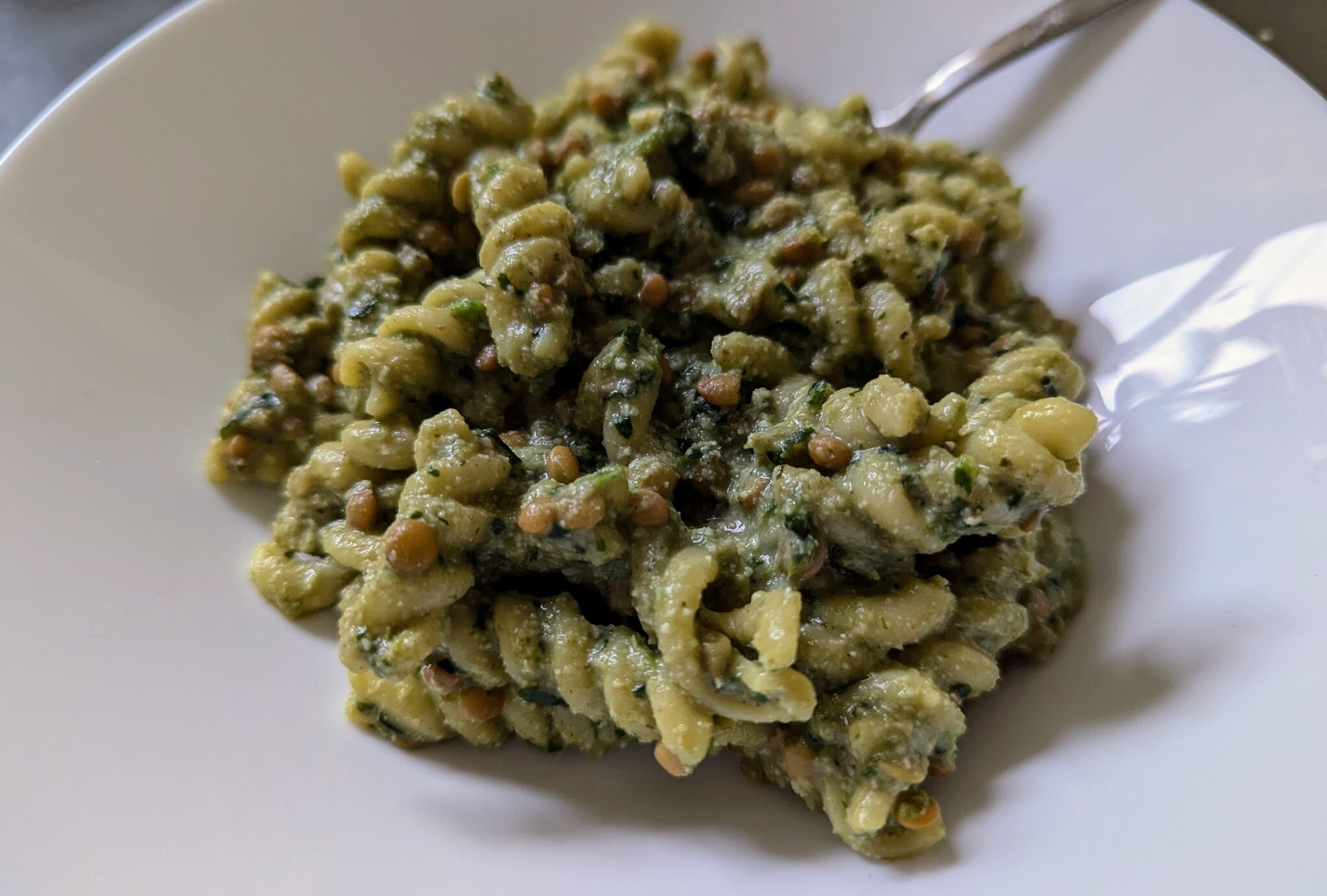 spiral pasta noodles covered in a green sauce on white plate.