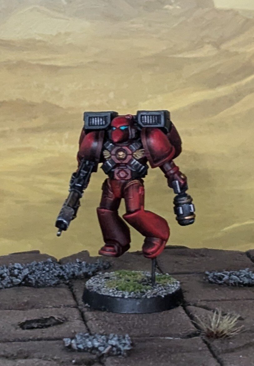 A photograph of a painted Warhammer 40,000 miniature. Red armored Blood Angel with a flamer and melta bomb.