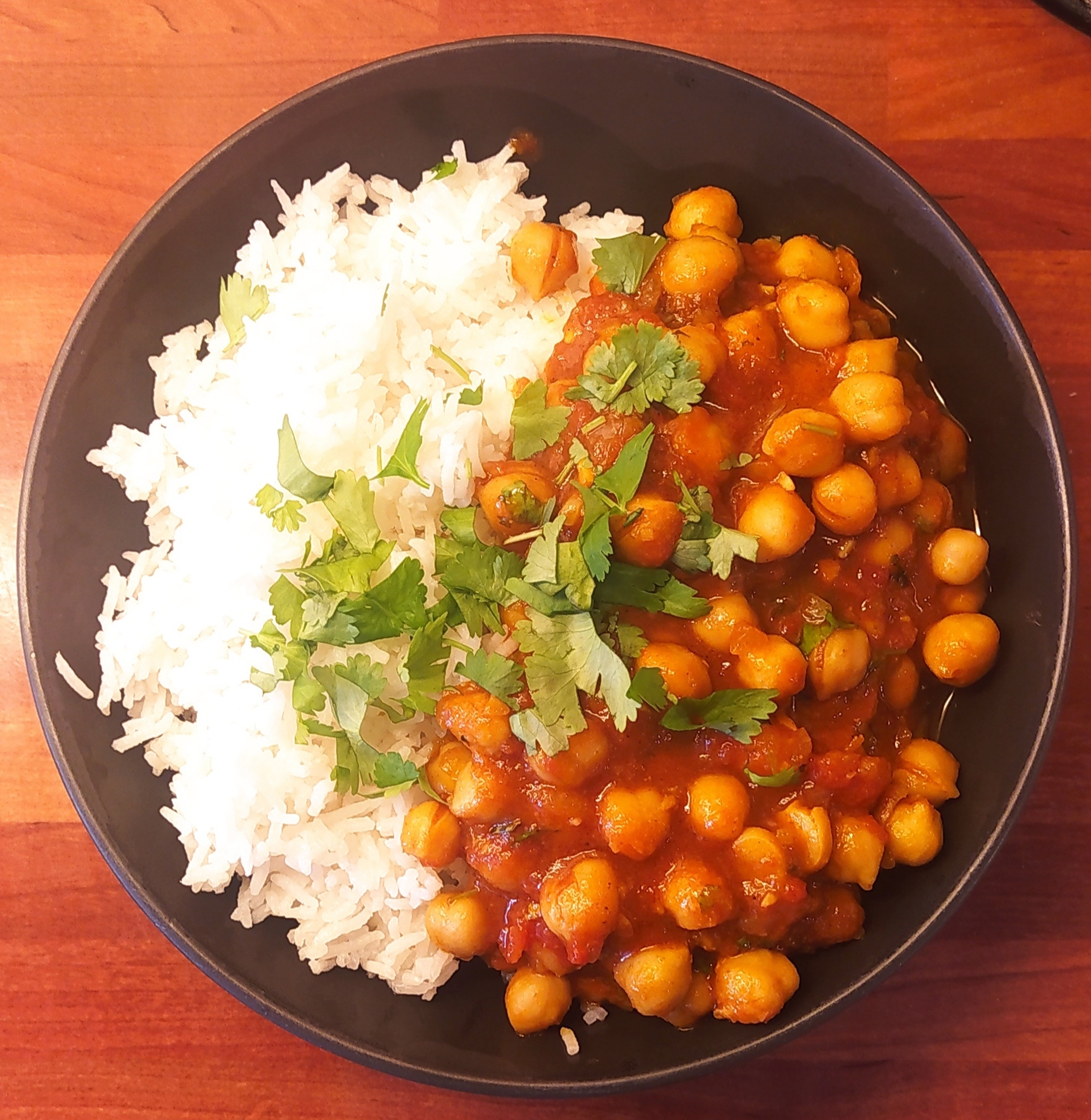 A plate of chananmasala over rice, garnished with chopped cilantro 